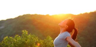 A woman standing outdoors with arms outstretched against a sunset backdrop