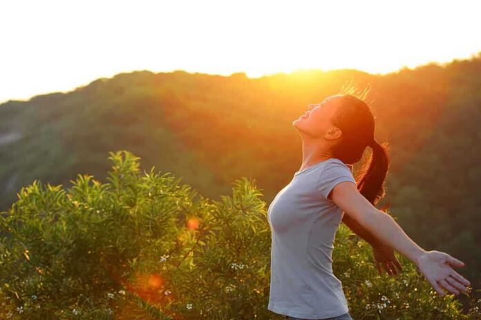 A woman standing outdoors with arms outstretched against a sunset backdrop