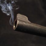 Close-up of a gun barrel emitting smoke against a black background