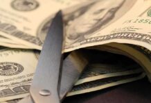 Scissors cutting through a stack of dollar bills