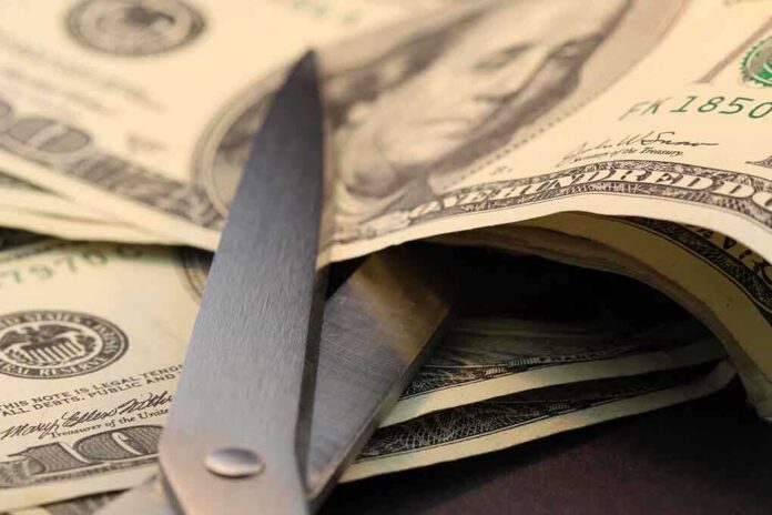 Scissors cutting through a stack of dollar bills