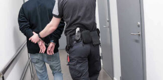 Officer escorting handcuffed person down hallway.