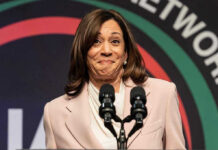 Woman smiling behind two microphones on a podium.