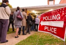 People waiting in line at a polling place with a sign indicating direction