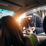 Masked criminal reaching through car window attempting to rob occupants inside vehicle on rainy day