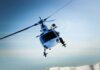 A helicopter flying over a mountainous landscape against a blue sky