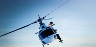 A helicopter flying over a mountainous landscape against a blue sky