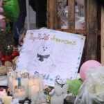 A memorial site with candles, flowers, and a hand-drawn poster
