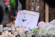 A memorial site with candles, flowers, and a hand-drawn poster