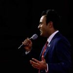 Man in a suit speaking into a microphone on stage