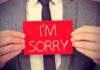 A man in a suit holding a red sign that says IM SORRY