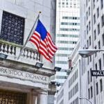 Facade of the New York Stock Exchange with an American flag and Wall Street sign