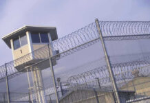 Execution Frenzy — Washington Looks Away Guard tower behind barbed wire fence in a prison.