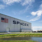 Massive Wealth Jump Sparks Fight Over New Tax Rules SpaceX building with American flag and launch pad.