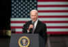 Sudden Health Fear Reopens Fitness Debate Man speaking at podium with US flag background.