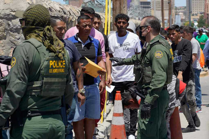 2300859029-1 Border patrol agents inspecting group of individuals in line.