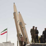 Tehran Power Grab — President Tries To Quit Military personnel beside missiles and Iranian flag.