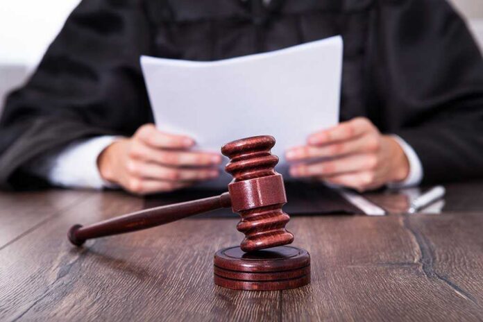 Close-up,Of,Male,Judge,In,Front,Of,Mallet,Holding,Documents A judge holding documents with a gavel in the foreground