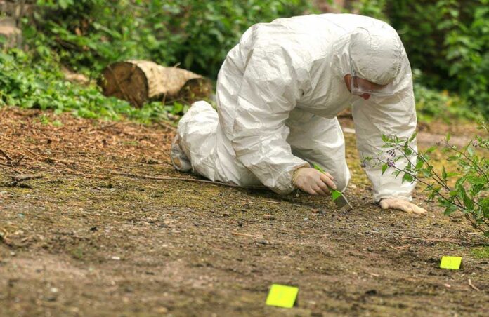 Criminologist,Investigates,A,Crime,Scene Forensic investigator in a protective suit collecting evidence from the ground