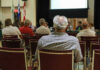 The event is back. The controversy isn’t over. People attending a meeting in a conference room.