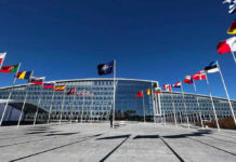 The vote is over. The debate is just beginning. Flags outside NATO headquarters building under clear blue sky.