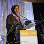 Woman in hijab speaking at a podium on a decorated stage