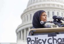 America’s 250th Anniversary Becomes the Latest Battleground Woman in hijab speaking at podium with microphones outside a domed building