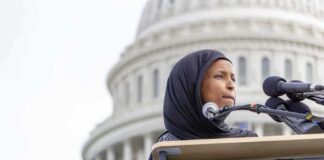 Woman in hijab speaking at podium with microphones outside a domed building