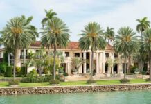 A luxurious mansion surrounded by palm trees and a waterfront view