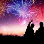 Silhouetted figures enjoying a fireworks display against a colorful night sky