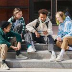 Viral Streamer Tells Teen Boys to Smash Their Faces With Hammers Group of teens sitting on outdoor steps looking at a phone