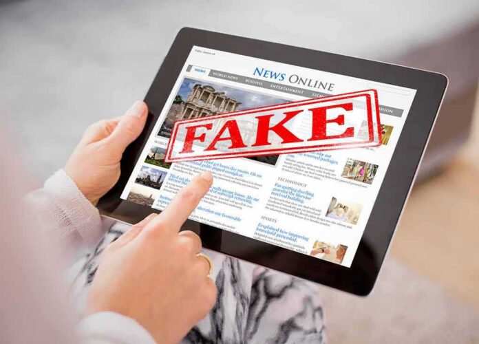 shutterstock_675861955-1- Person holding a tablet displaying a news website with a 'FAKE' stamp