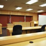 Once a Voice Against Beijing, Now Serving 30 Years for Fraud Interior view of an empty courtroom with wooden furniture and American flags