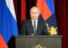 Putin Has No Named Successor at 73 man in suit speaking at a podium with flags behind him