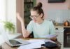 Oz Targets California Unions Over Medicaid Fraud Young woman with glasses frustrated at laptop while holding bills
