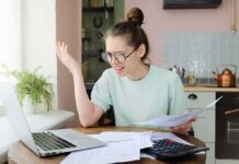Young woman with glasses frustrated at laptop while holding bills