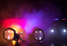 Clown Costume Teen Shocks 78-Year-Old Murder Investigation Handcuffs on a surface with police cars and flashing lights in smoky darkness