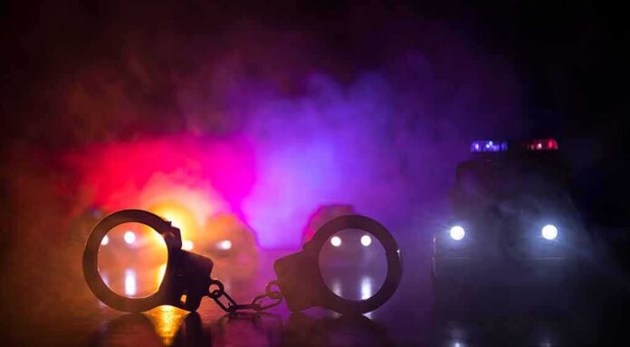 Handcuffs on a surface with police cars and flashing lights in smoky darkness