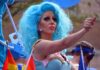 7 Days to End Secret Gender Transitions Drag performer with bright blue wig giving thumbs up at parade