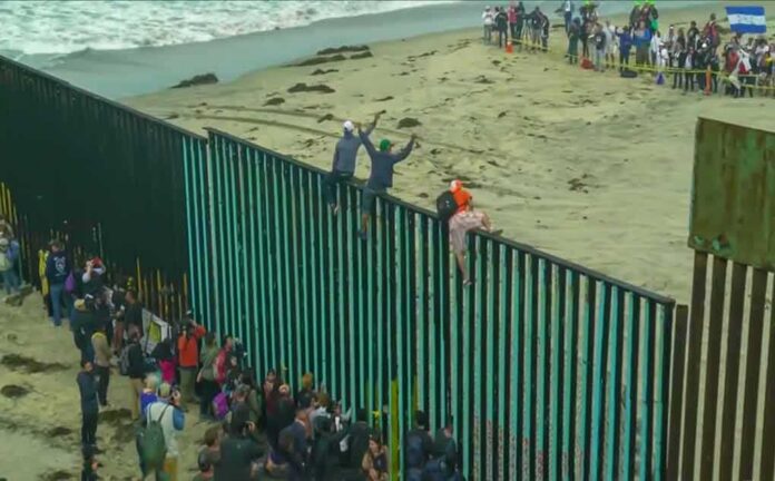 People climbing a tall beachside border fence
