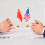 Two diplomats sit across table with China and United States flags between them