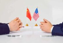 Two diplomats sit across table with China and United States flags between them