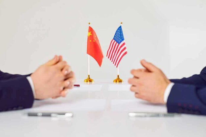 shutterstock_2169636285 Two diplomats sit across table with China and United States flags between them
