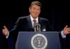 man at presidential podium gesturing with arms open