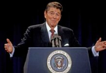 man at presidential podium gesturing with arms open