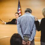 Defendant in handcuffs stands before a judge in a courtroom