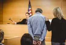 Hidden for Years: Mother Found in Living Room Freezer Defendant in handcuffs stands before a judge in a courtroom