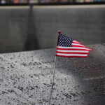 Patriot Day Turns 25: A New Generation Remembers American flag on a rainy memorial nameplate.