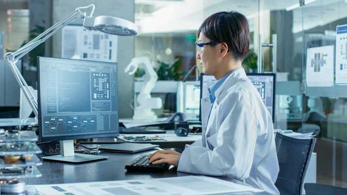 shutterstock_1104131792-1 Engineer in lab coat working at a computer in a modern lab