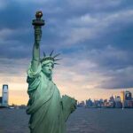 Fatal Harbor Ride Sparks Charges Statue of Liberty with city skyline at dusk